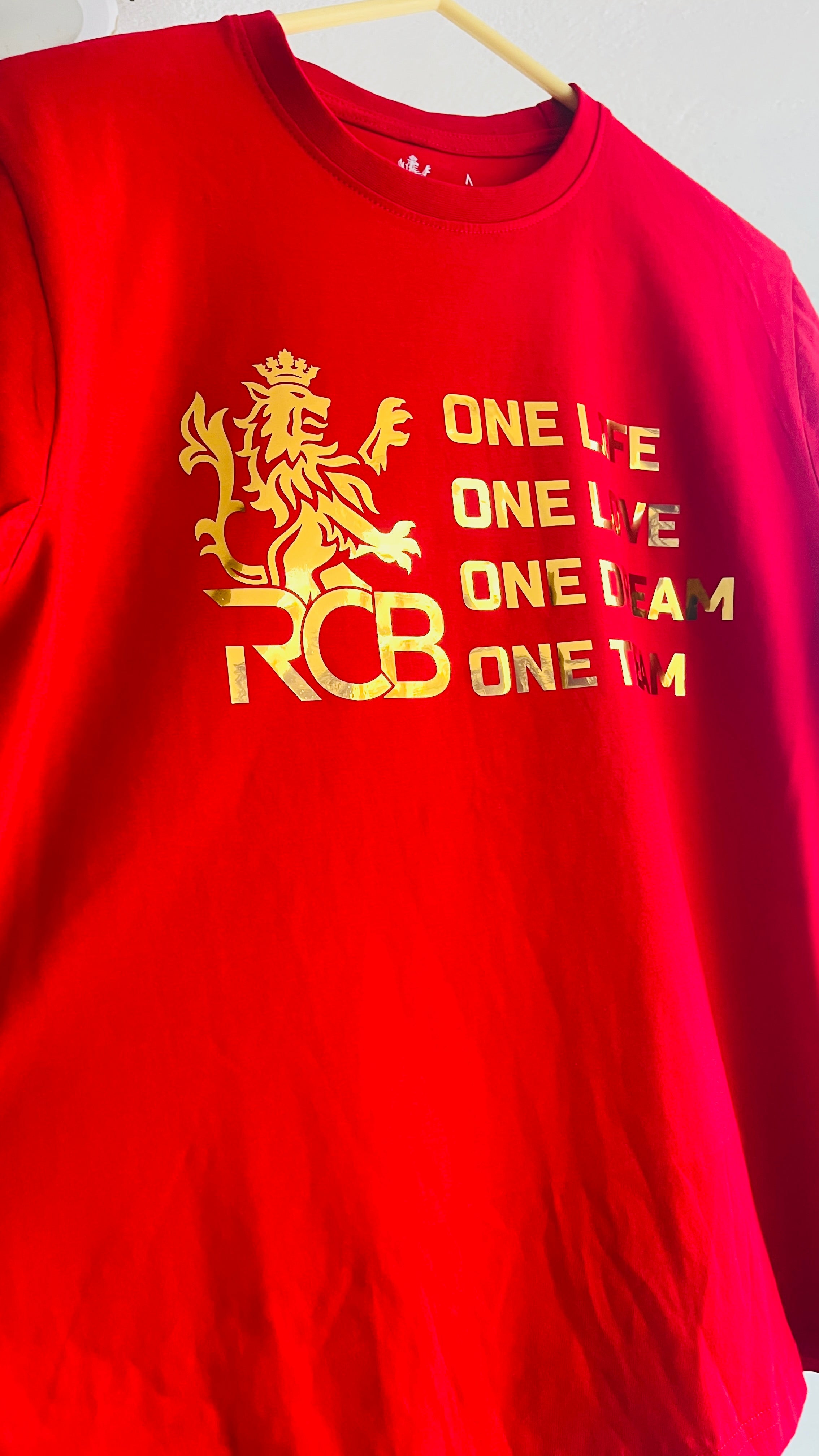 Royal Challengers Bangalore RCB red T-shirt with gold print lion logo and “One Life One Love One Dream One Team” slogan