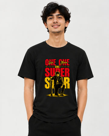 A man wearing a black short-sleeve t-shirt with a red and yellow graphic print on the front that reads 'ONE ONE and ONE SUPER STAR' with an illustration of a seated figure. The photo is taken against a plain light gray studio background.