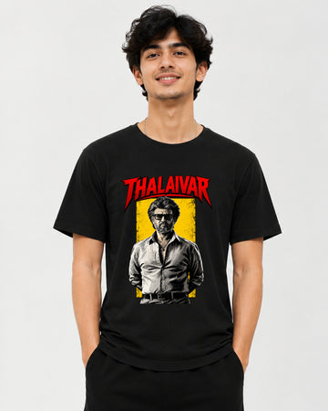 A man wearing a black graphic t-shirt featuring a red 'THALAIVAR' logo and a stylized portrait of Thalaivars on a yellow background, set against a plain light gray studio backdrop.